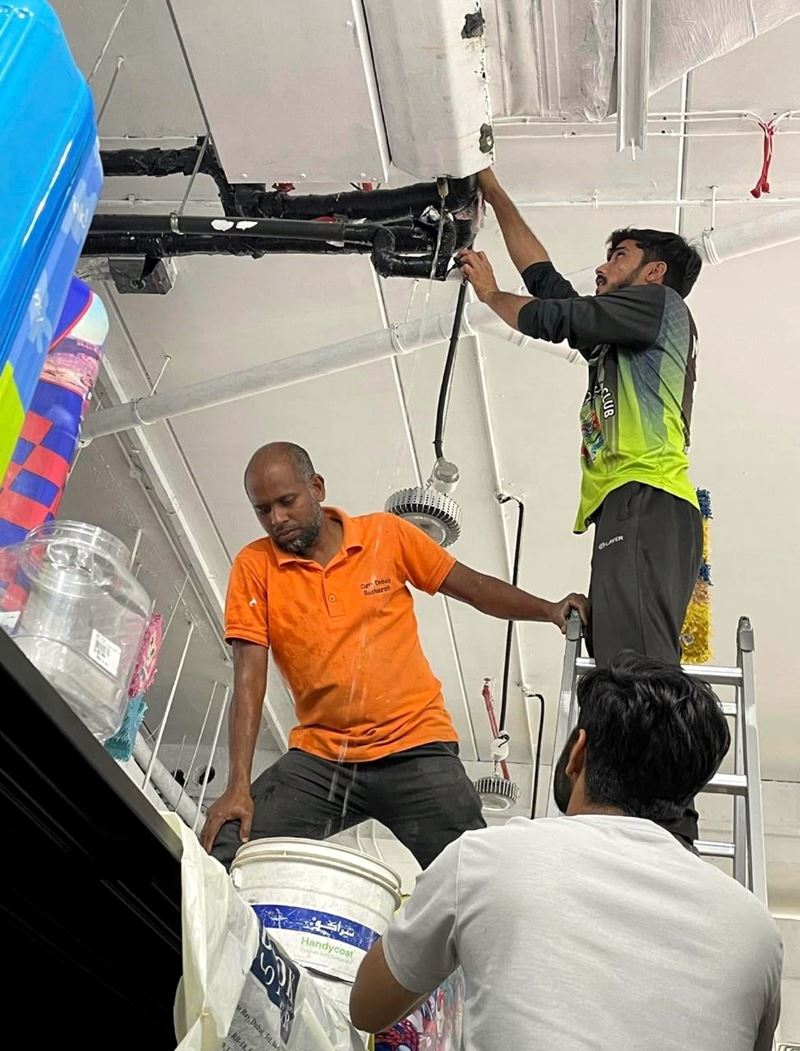 Technicians servicing a ceiling-mounted AC unit from a ladder