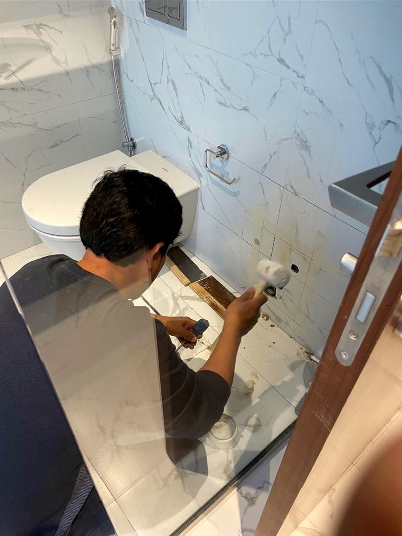 Technician replacing bathroom tiles to access plumbing