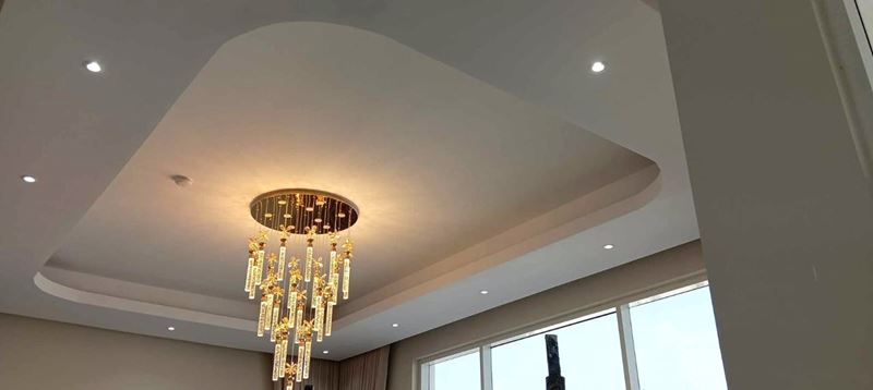 Layered gypsum ceiling with recessed downlights and a crystal chandelier above a double-height room