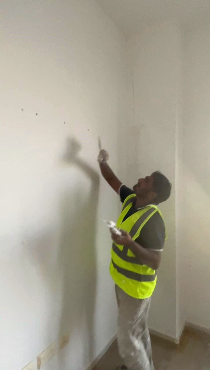 Painter in a high-visibility vest preparing an interior wall